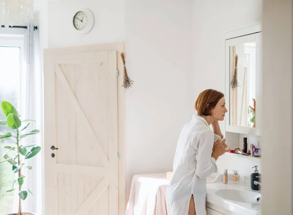 A young woman putting on a make-up in the morning in a bathroom. — Stock Photo, Image