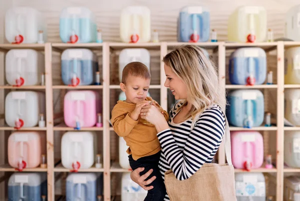 En ung kvinna med ett barn pojke att köpa vätskor i noll avfall shop. — Stockfoto