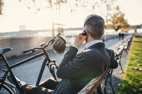 Affärsman pendlare med cykel sitter på bänken i city, lyssna på musik. — Stockfoto