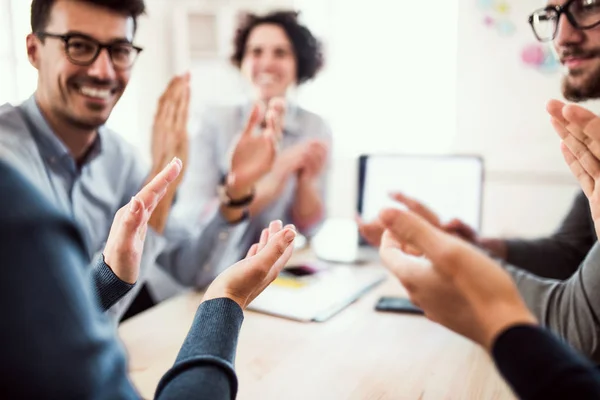 Grupo de jóvenes empresarios sentados alrededor de la mesa en una oficina moderna, aplaudiendo . — Foto de Stock