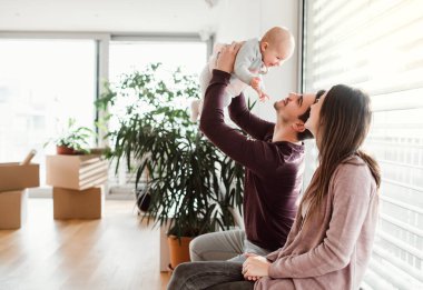 Bir bebek ve karton kutular içinde yeni bir ev taşıma ile genç çift portresi.