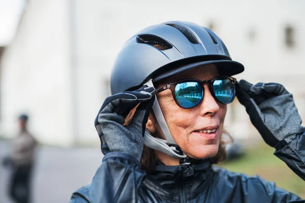 Etkin bir üst düzey kadın ayakta açık havada, güneş gözlüğü üzerinde koyarak Bisiklet kask ile. — Stok fotoğraf