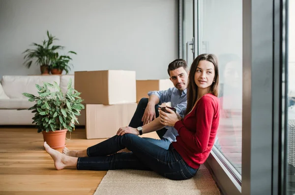 Jeune couple avec des boîtes en carton se déplaçant dans une nouvelle maison, assis sur un sol . — Photo