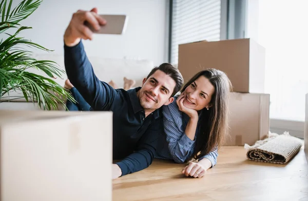 A young couple with a smartphone moving in a new home, taking selfie. — Stock Photo, Image