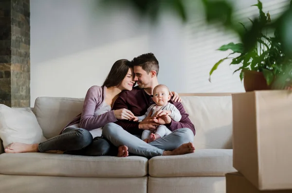 Un retrato de pareja joven con un bebé y cajas de cartón moviéndose en un nuevo hogar . — Foto de Stock