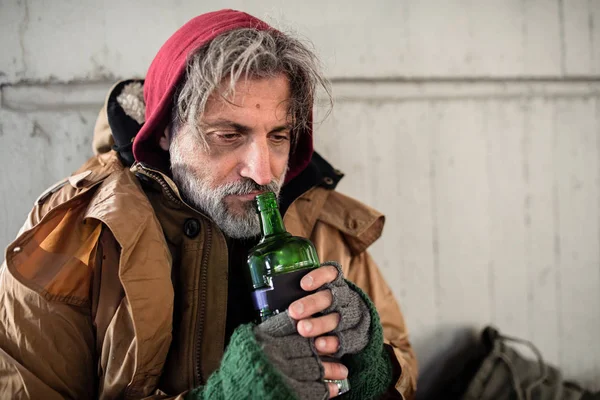 Vue de face d'un mendiant sans abri assis à l'extérieur, tenant une bouteille d'alcool. Espace de copie . — Photo