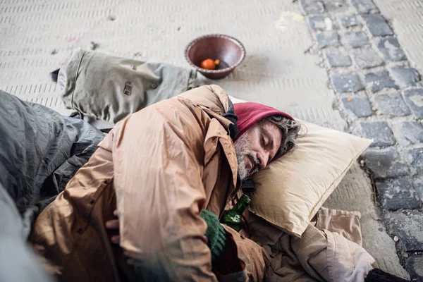 Dakloze bedelaar man liggend op de grond buiten in de stad, slapen. — Stockfoto