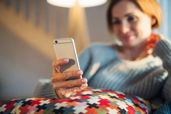 Smartphone kullanarak kapalı evde kanepede oturan genç bir kadın. — Stok fotoğraf