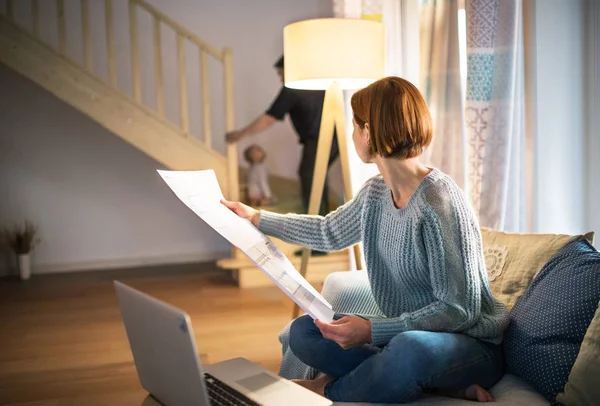 Junge Frau mit Laptop und Bauplänen, die drinnen sitzt und zu Hause arbeitet. — Stockfoto
