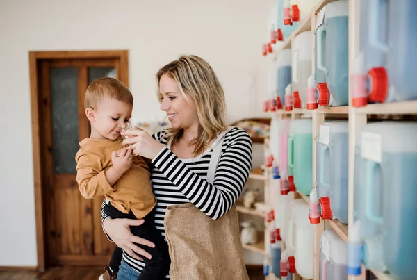 En ung kvinna med ett barn pojke att köpa vätskor i noll avfall shop. — Stockfoto