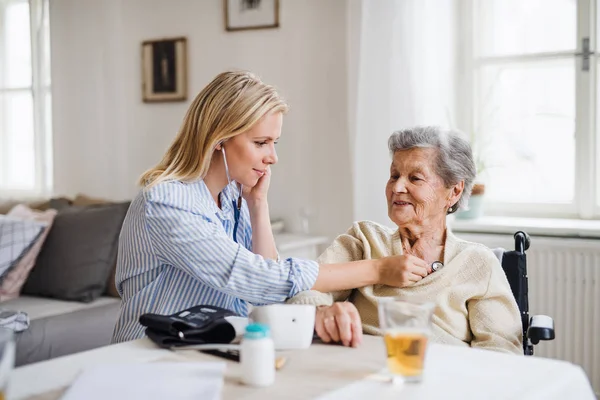 En hälsa besökare att granska en senior kvinna med stetoskop hemma. — Stockfoto