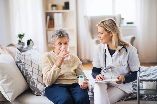 Eine Besucherin und eine Seniorin zu Hause, die Tabletten einnimmt. — Stockfoto