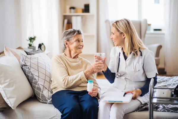 En hälsa besökare ger en senior kvinna ett glas vatten att ta piller. — Stockfoto