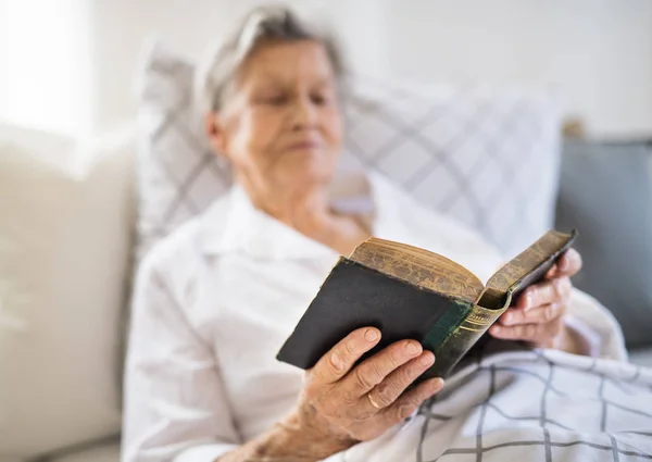 Sick senior woman reading bible book in bed at home or in hospital. — Stock Photo, Image