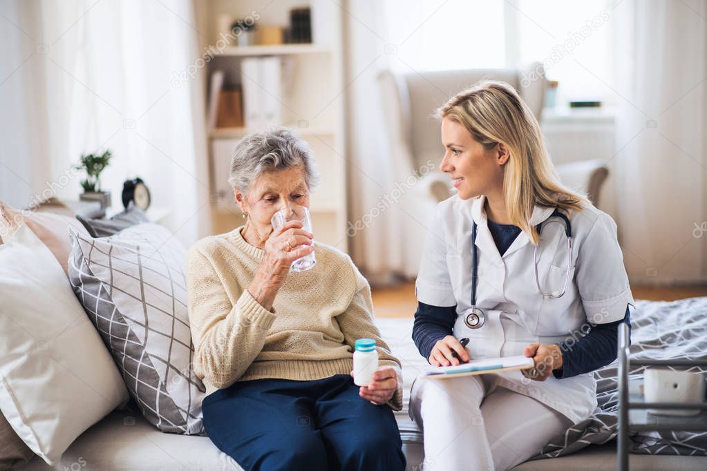 A health visitor and a senior woman at home, taking pills.