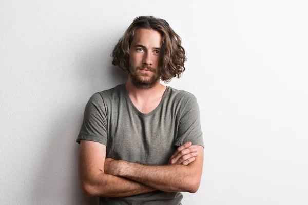 Portrait of a joyful young man with long wavy hair in a studio arms crossed. — Stock Photo, Image