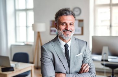 Mature businessman standing in an office, arms crossed.