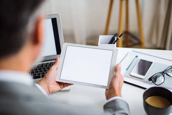 Um meio-termo de um homem de negócios sentado à mesa, usando um tablet. Uma visão traseira. Espaço de cópia . — Fotografia de Stock