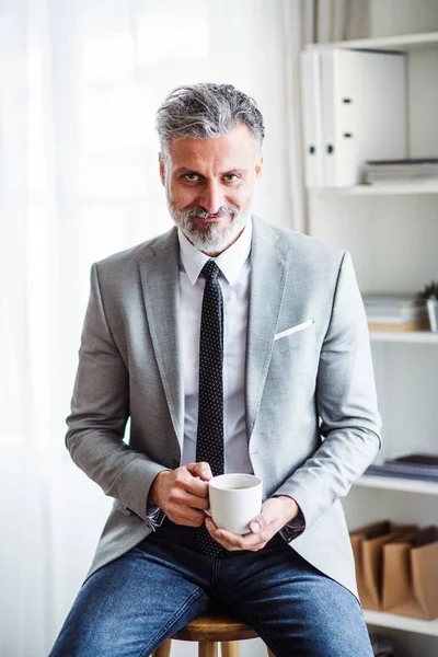 Un uomo d'affari maturo seduto in un ufficio, con in mano una tazza di caffè . — Foto Stock