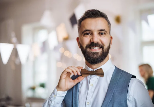 Portrait d'un homme mature debout à l'intérieur d'une fête, tenant un nœud papillon en bois . — Photo