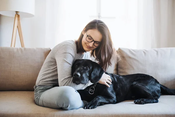 Tonårig flicka sitter på en soffa inomhus, leker med en hund. — Stockfoto