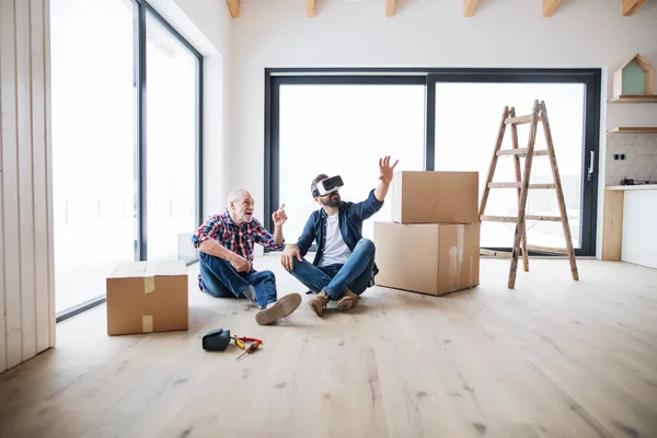 Un hombre con gafas VR y su padre mayor decorando una casa nueva, un nuevo concepto de hogar . —  Fotos de Stock