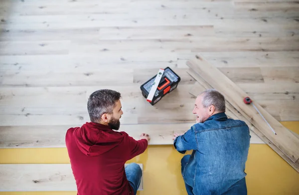 Un uomo maturo con il padre anziano che posa pavimenti in legno, un nuovo concetto di casa . — Foto Stock