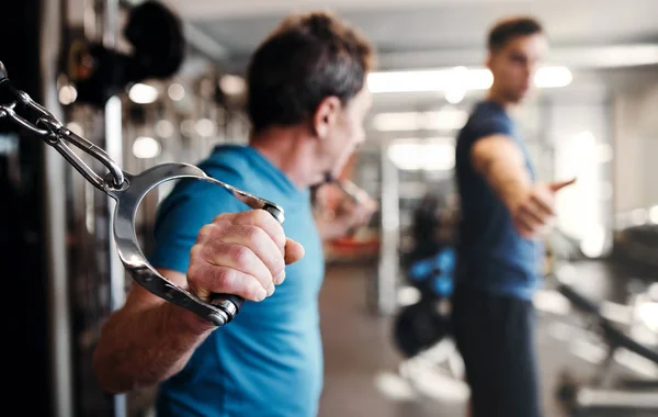 Un uomo anziano con un giovane allenatore che fa esercizio di allenamento di forza in palestra . — Foto Stock