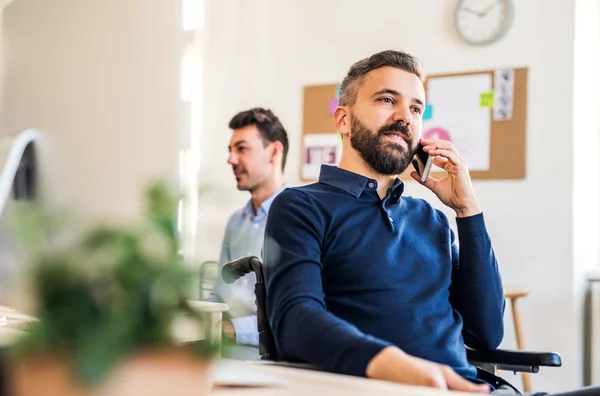 Joven hombre de negocios en silla de ruedas con smartphone trabajando en una oficina moderna . — Foto de Stock