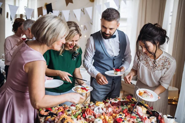 Familia multigeneracional poniendo comida en platos en una fiesta de cumpleaños familiar en interiores . —  Fotos de Stock