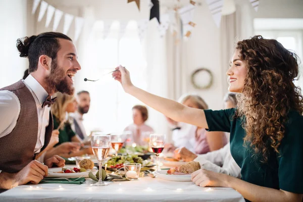 Um jovem casal sentado em uma mesa em uma festa de aniversário indoor, uma mulher alimentando um homem . — Fotografia de Stock