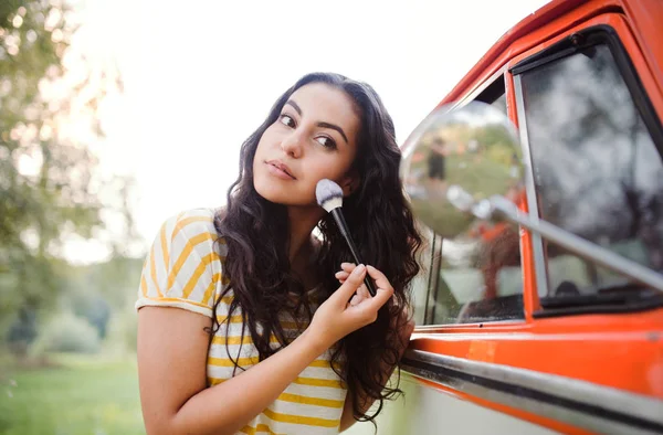 A girl looking in mirror and applying makeup on a roadtrip through countryside.