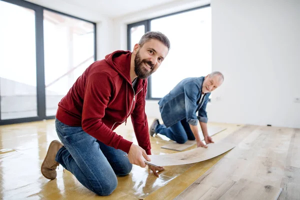 Een volwassen man met zijn senior vader legdatum vinyl vloerbedekking, een nieuwe home concept. — Stockfoto