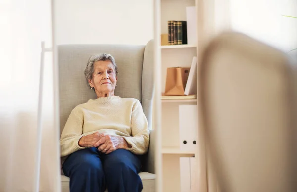 Ett porträtt av en äldre kvinna sitter hemma, tittar på kameran. Kopiera utrymme. — Stockfoto