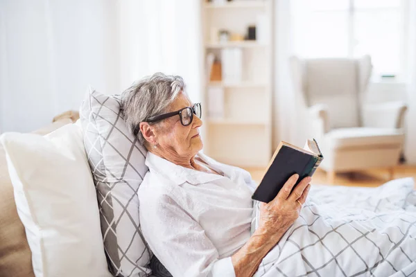 Sick senior woman reading bible book in bed at home or in hospital. — Stock Photo, Image