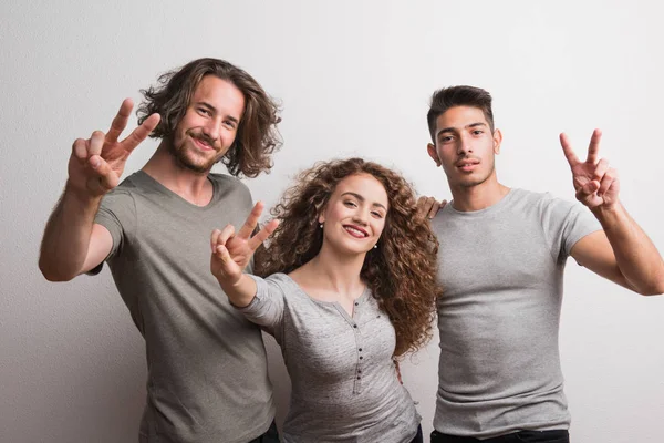 Ritratto di giovane ragazza gioiosa con due amici maschi in piedi in uno studio, V per la vittoria . — Foto Stock