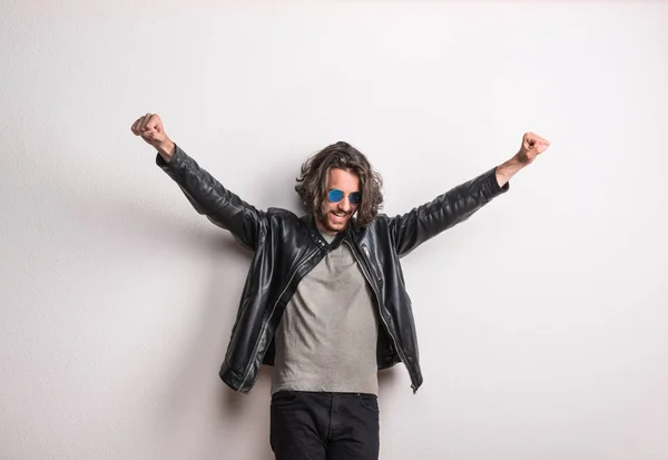 Portrait of a young man with sunglasses and leather jacket in a studio, arms stretched. — Stock Photo, Image