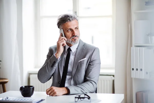 Grave uomo d'affari maturo con smartphone seduto a tavola, fare una telefonata . — Foto Stock