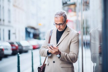 Şehirde bir sokakta duran, smartphone tutan olgun iş adamı.