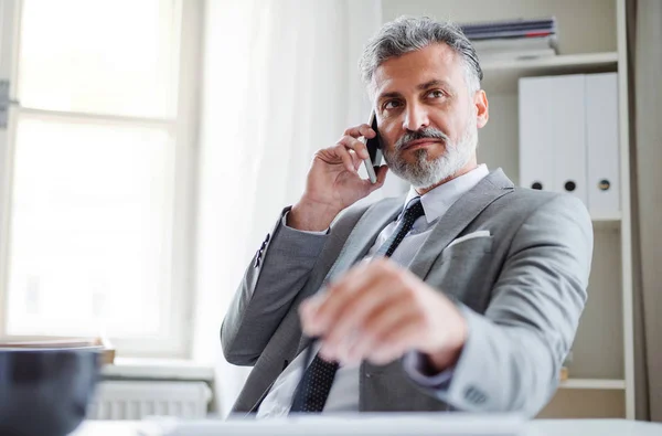 Seriös mogen affärsman med smartphone som sitter vid bordet, att ringa ett telefonsamtal. — Stockfoto