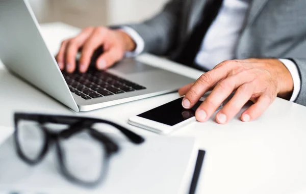 En midsection affärsman med smartphone och laptop sitter vid bordet, arbetar. — Stockfoto