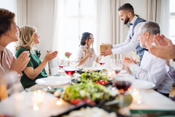 Un homme offrant un cadeau à une jeune femme surprise lors d'une fête d'anniversaire de famille . — Photo