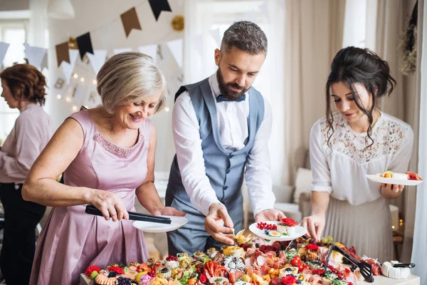 Familia multigeneracional poniendo comida en platos en una fiesta de cumpleaños familiar en interiores . —  Fotos de Stock