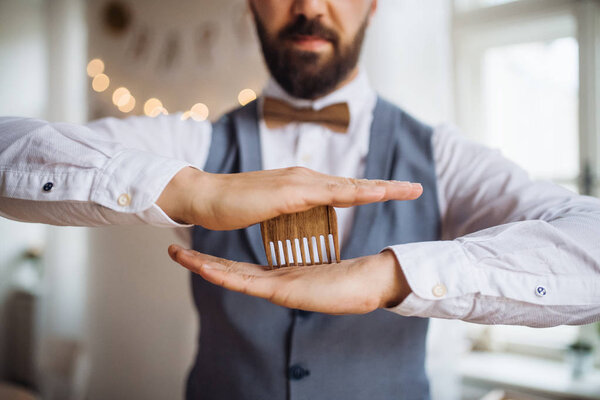 Midsection of man standing indoors in a room set for a party, holding a beard comb.