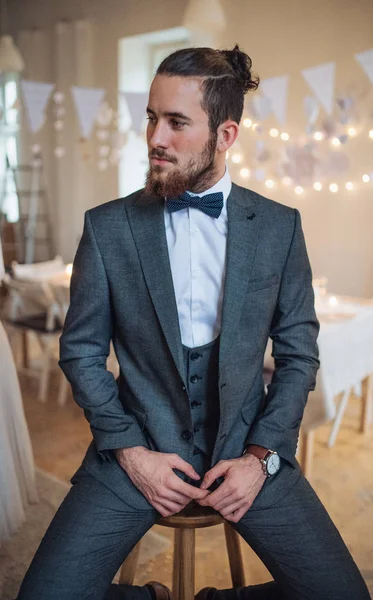 Ein hübscher junger Hipster mit formalem Anzug sitzt auf einem Schemel auf einer Indoor-Party. — Stockfoto