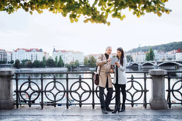 Hombre y mujer socios de negocios con la tableta de pie junto a un río en la ciudad de Praga . — Foto de Stock