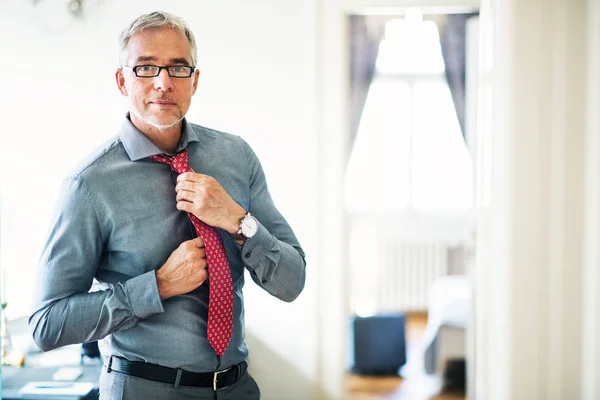 Rijpe zakenman op een zakelijke reis staande in een hotelkamer, aankleden. — Stockfoto