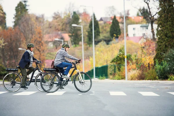 Aktives Seniorenpaar mit Elektrofahrrädern beim Überqueren einer Straße in der Stadt. — Stockfoto