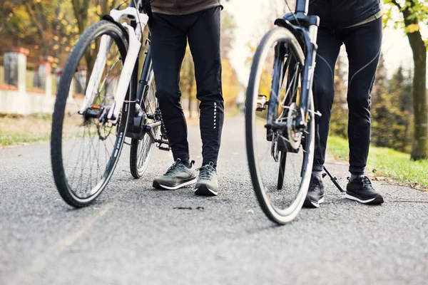 Beine und Füße eines Pärchens mit Elektrofahrrädern im Freien auf einer Straße im Park. — Stockfoto