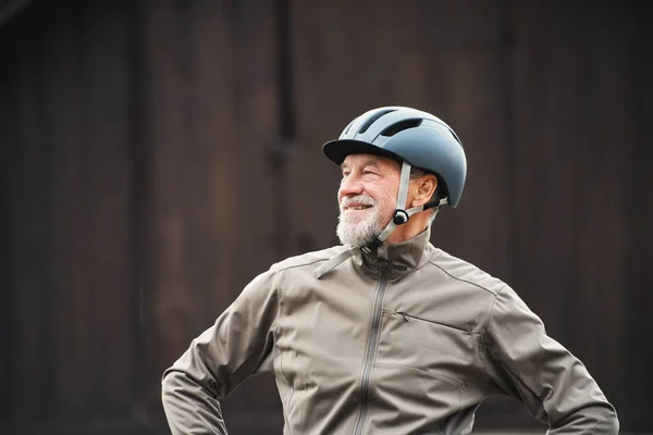 Aktiver Senior mit Fahrradhelm steht vor dunklem Hintergrund im Freien. — Stockfoto